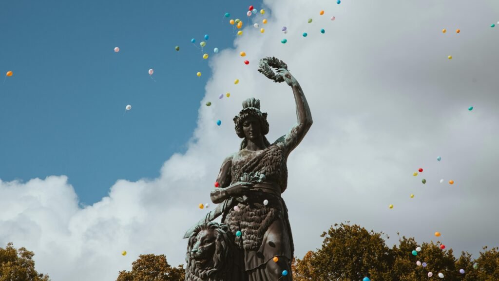 Statue of Bavaria in Munich with colorful balloons set against a cloudy sky.
